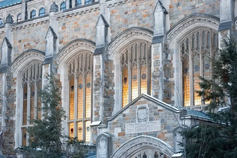 The Gothic stone facade of the University of Michigan Law Library, its tall leaded windows lit at dusk.
